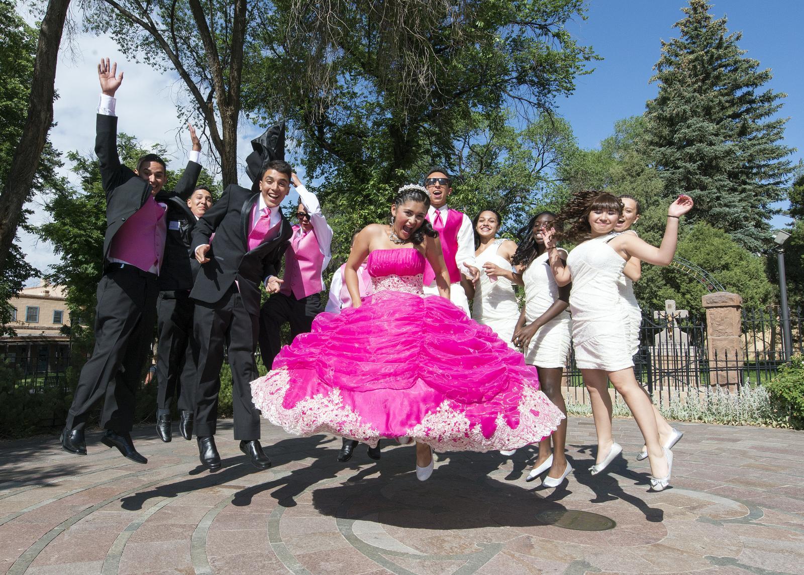 A group of people are posing for a picture with a girl in a quince dress.