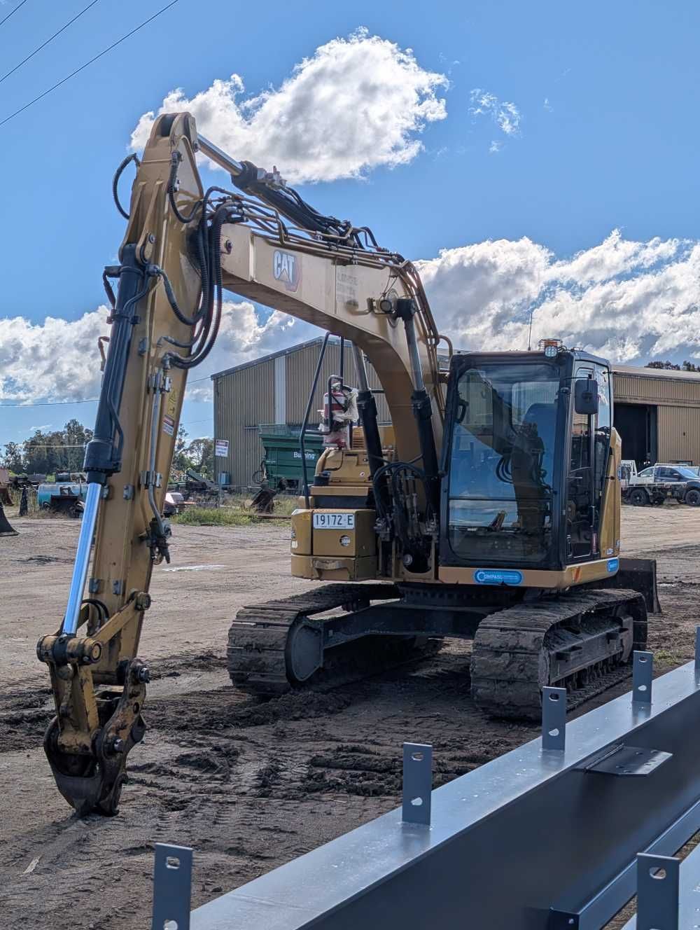 Yellow excavator parked on a dirt lot under a blue sky with clouds — Compass Equipment Hire in Tweed Heads, NSW
