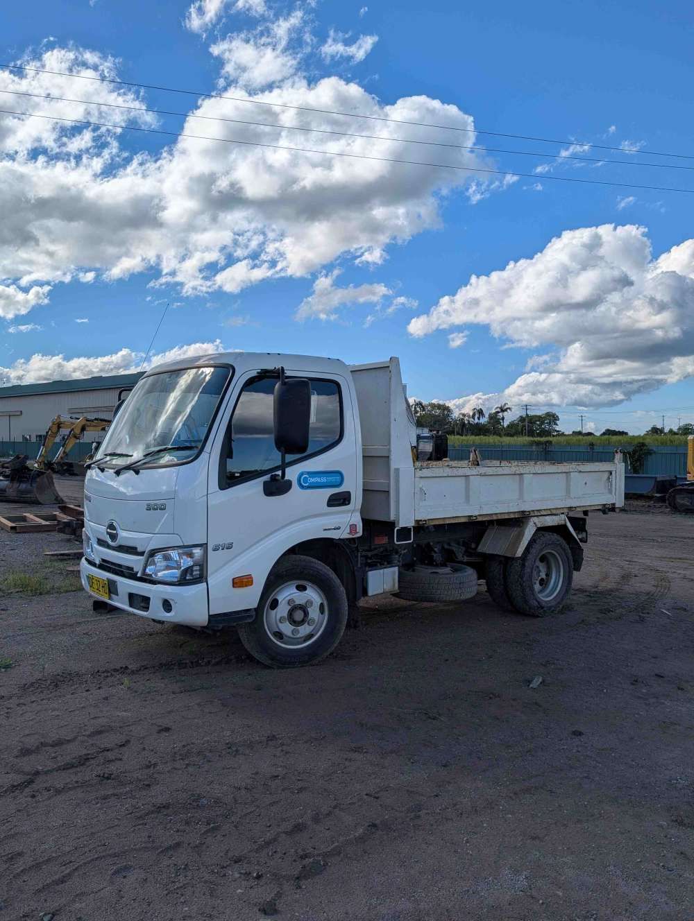 White dump truck parked on a gravel lot under a cloudy blue sky — Compass Equipment Hire in Tweed Heads, NSW
