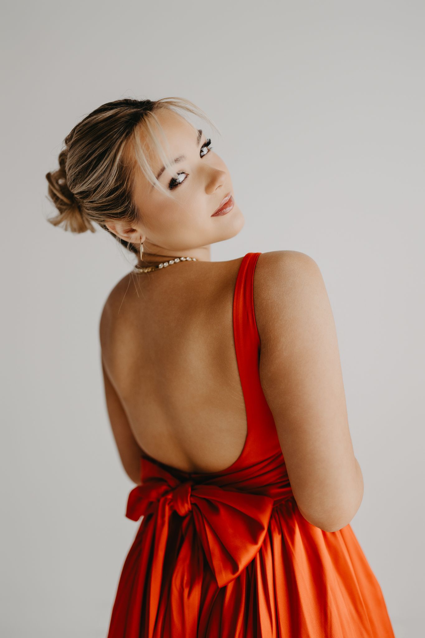 A person wearing a backless red dress with a large bow, looking over their shoulder against a plain light background.