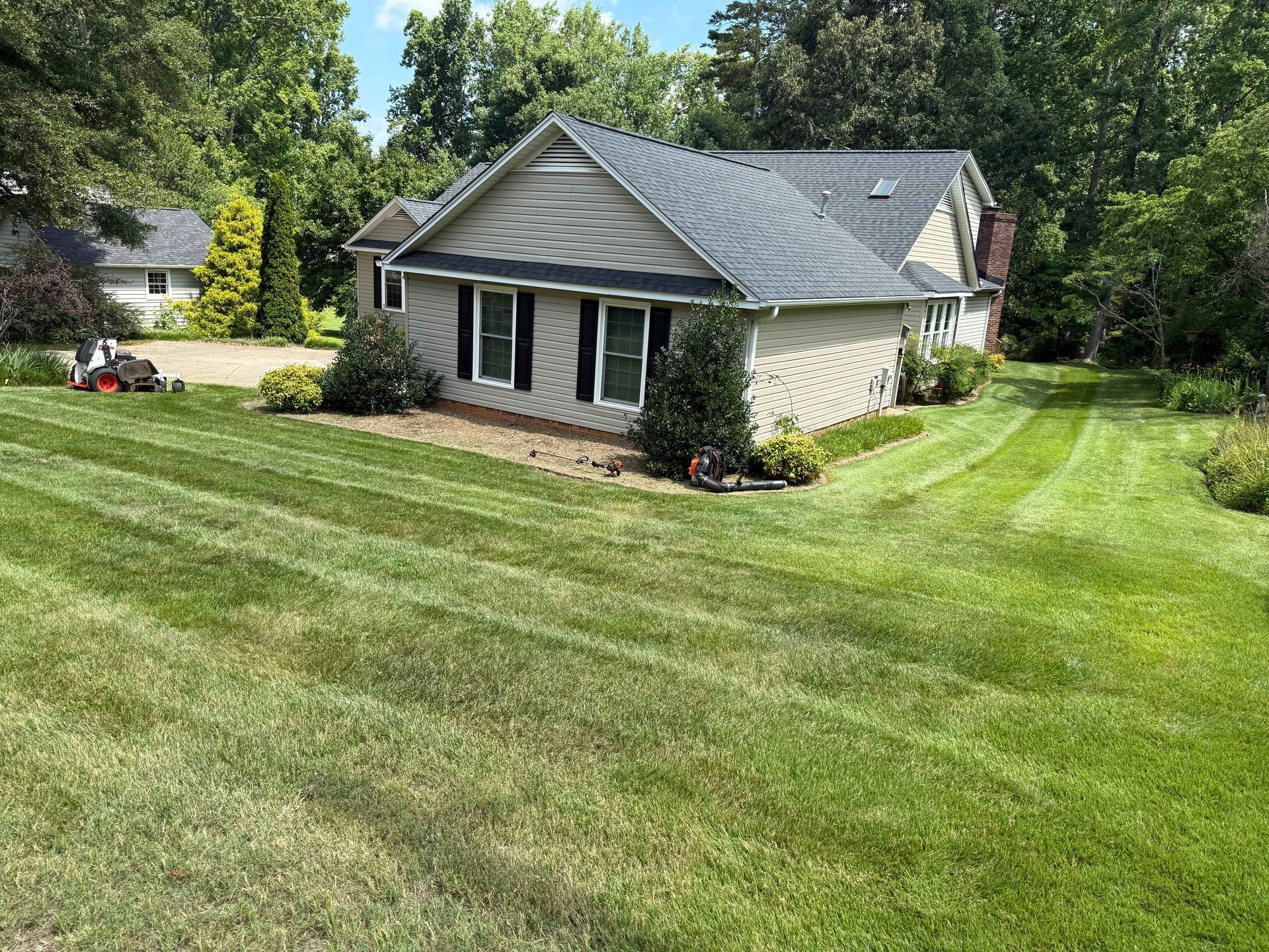House with freshly mowed green lawn. A riding lawn mower is in the background.