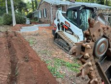 Bobcat skid steer with a trencher digging a trench near a house.