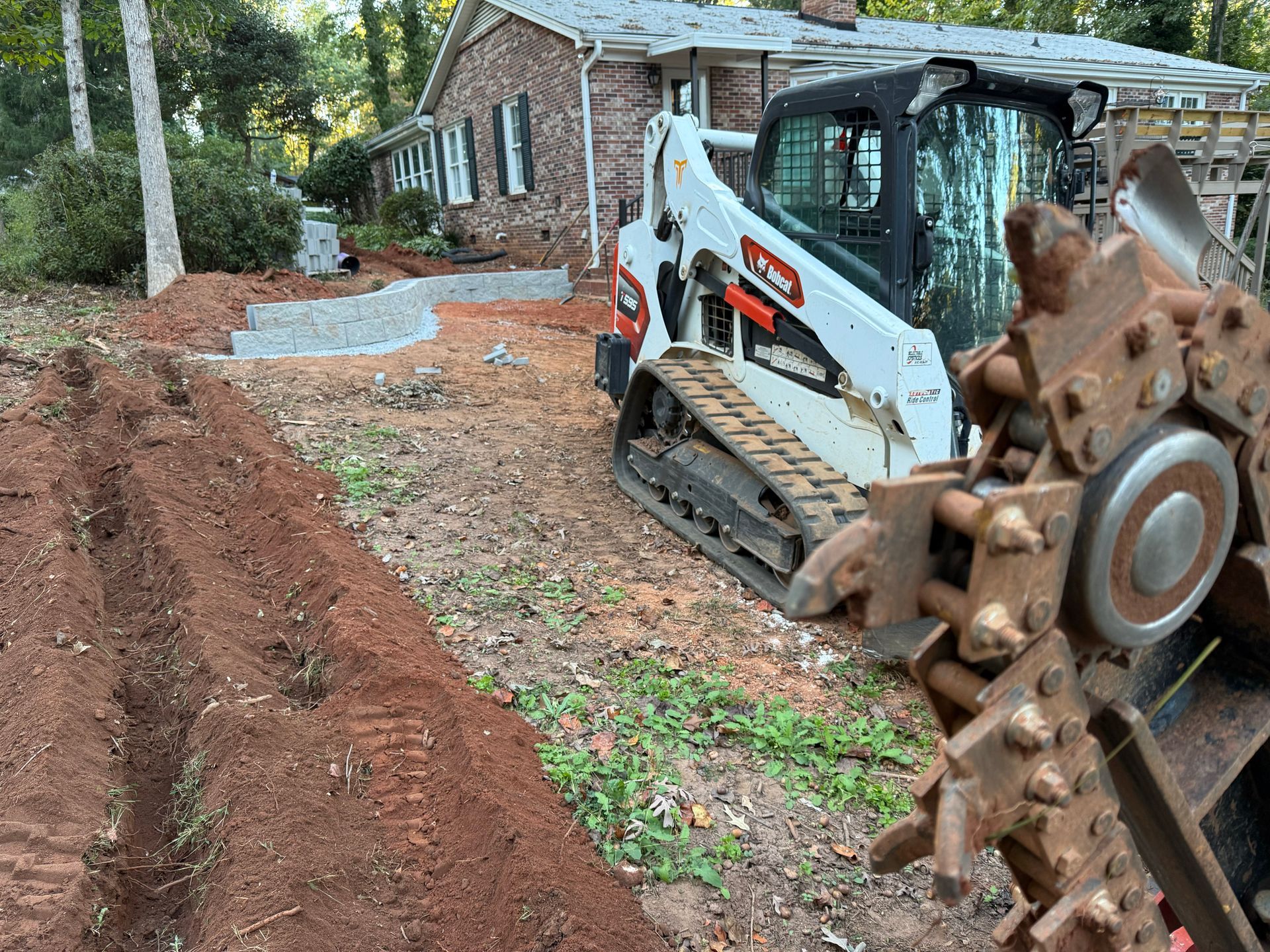 Bobcat excavator digging a trench near a house with red brick siding.