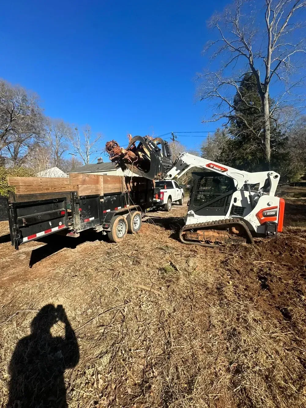 Bobcat loader filling a trailer with wood debris in a yard on a sunny day.