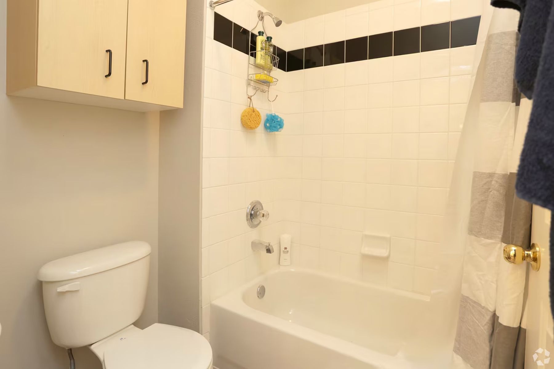 Student apartment bathroom at Milestone Stillwater featuring tub, tile surround, and storage cabinetry.