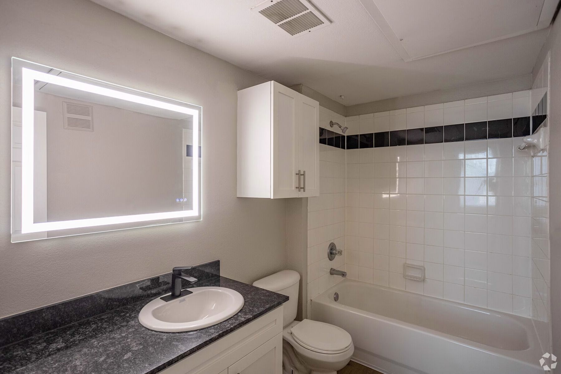 Updated bathroom at Milestone Stillwater with LED vanity mirror, dual sinks, and tiled shower.