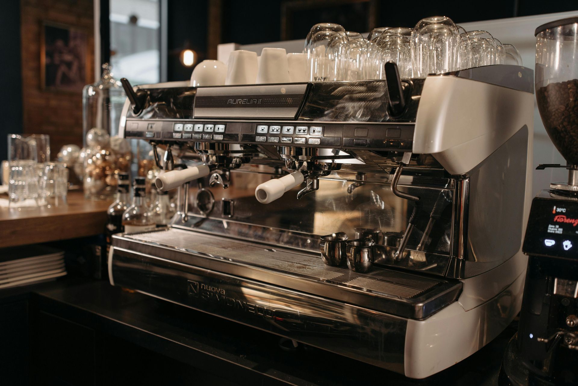 Espresso machine on a counter in a cafe; glasses and grinder nearby.