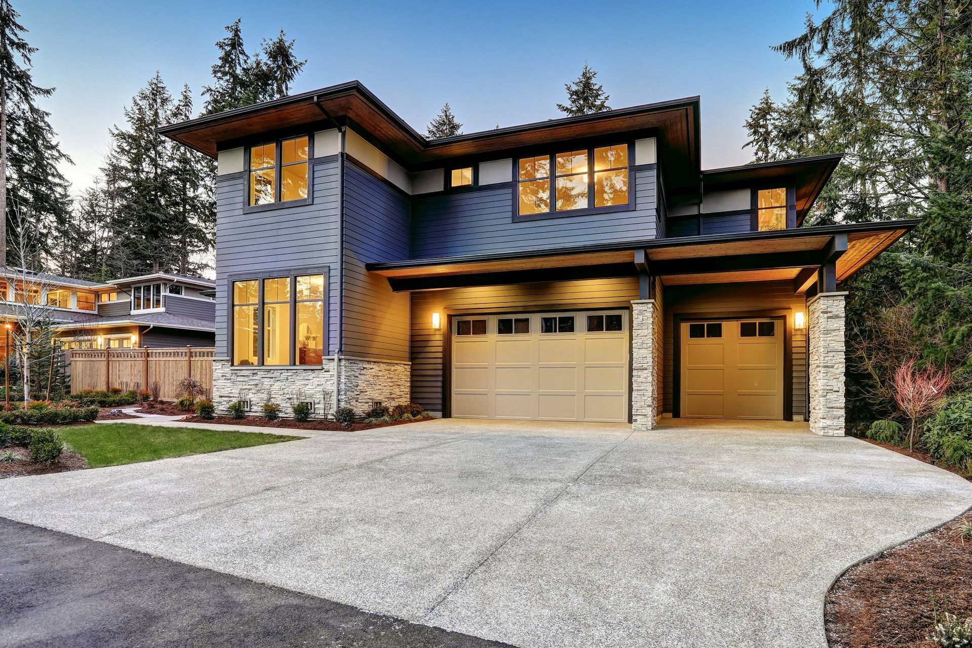 Modern two-story house with stone exterior, lit windows, and a double garage at dusk