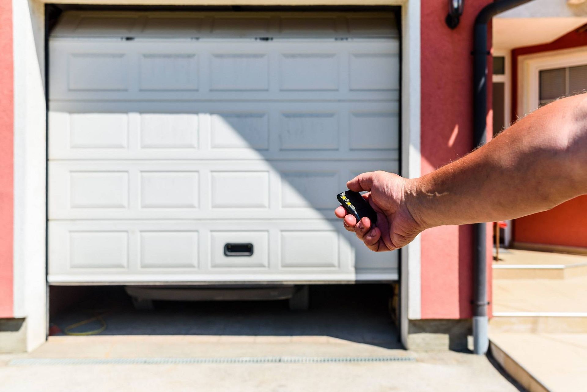 Hand holding a garage door remote aimed at a white garage door opening into a driveway