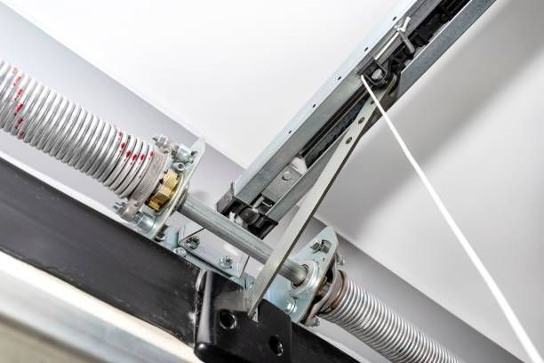 Close-up of a metal garage door spring and rail mechanism against a white ceiling.