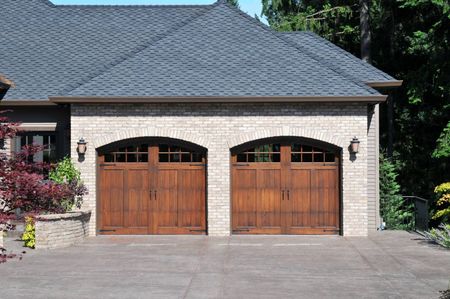 Two-car wooden garage doors beneath a gray shingled roof and stone exterior.