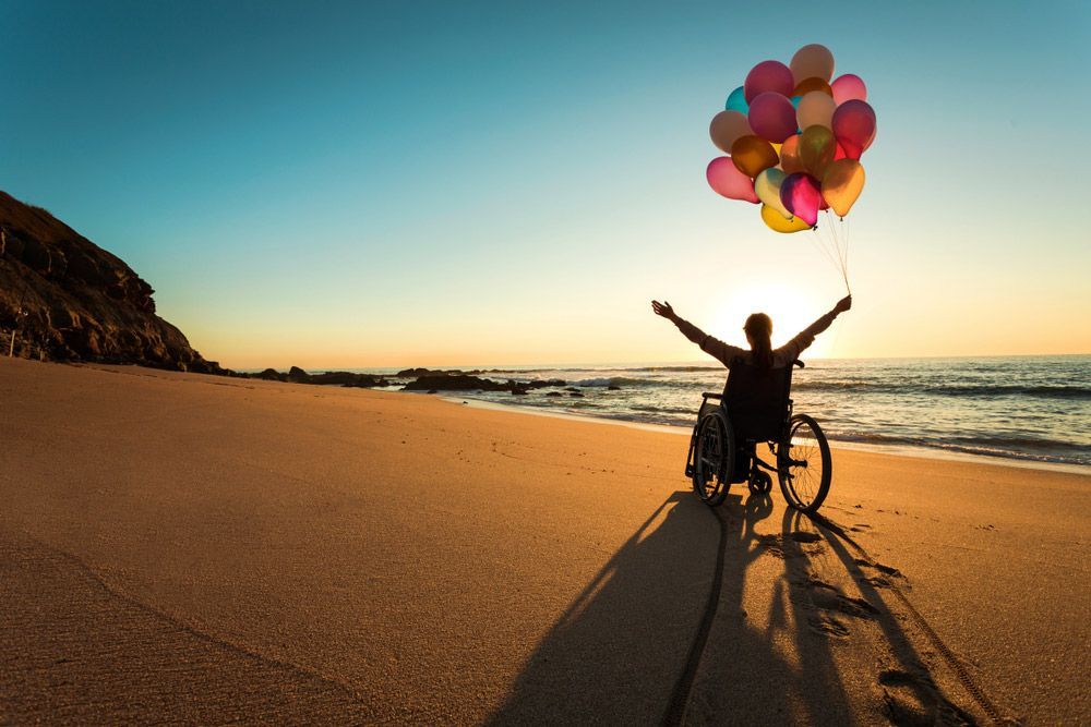 A Person in a Wheelchair is Holding Balloons on the Beach — Learn to Live in Annandale, QLD