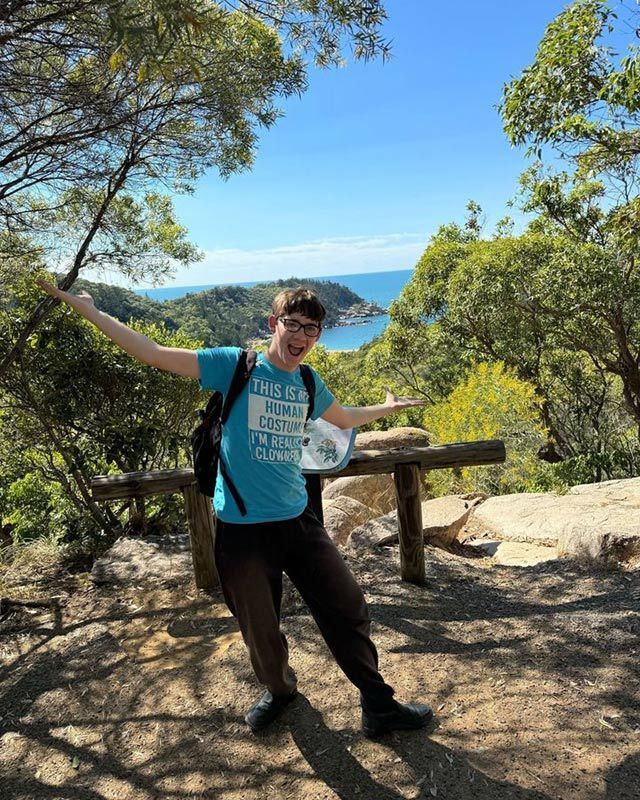 A Man in a Blue Shirt is Standing on Top of a Hill With His Arms Outstretched — Learn to Live in Currajong, QLD