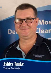 Man wearing glasses, smiling, in front of a blue sign that reads 