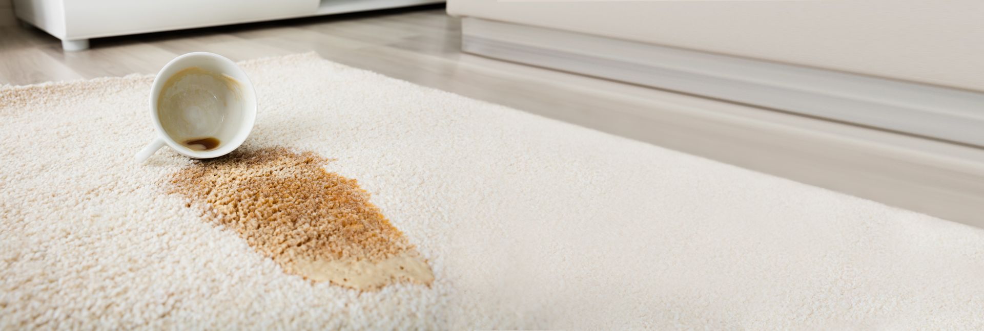 Spilled coffee on a white rug with an overturned cup.