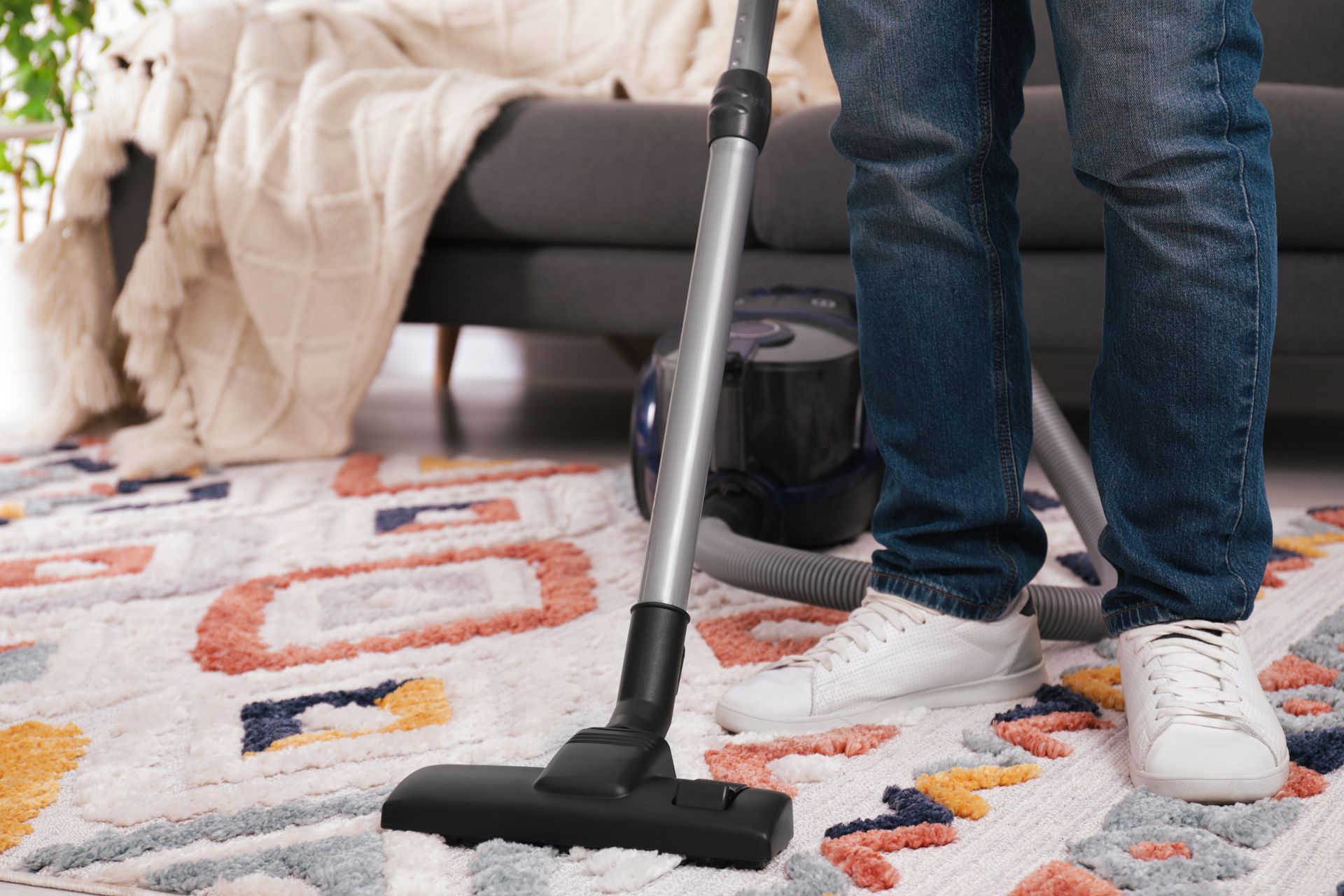 Person vacuuming a patterned rug with a vacuum cleaner, in a living room setting.