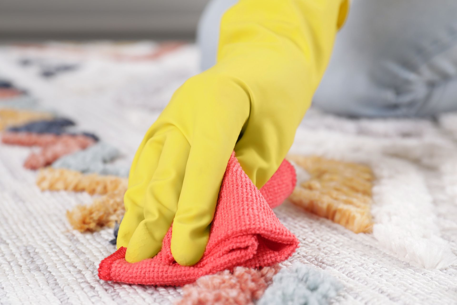 Person wearing yellow gloves wiping a colorful rug with a red cloth.