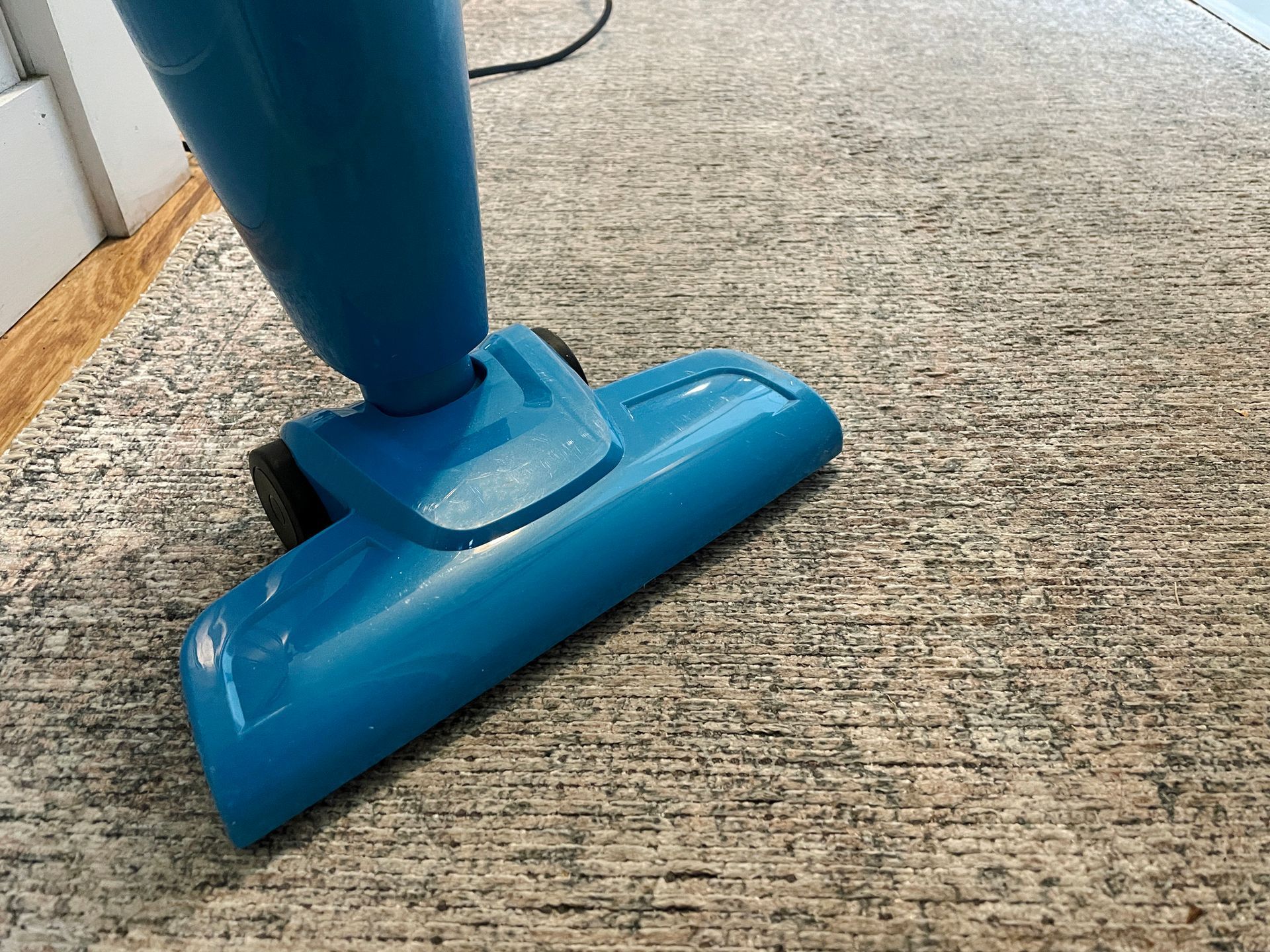 Blue steam cleaner head on patterned carpet.