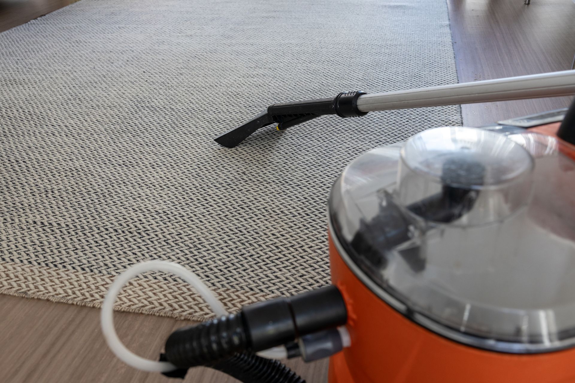 Orange carpet cleaner vacuuming a light-colored rug on a wooden floor.