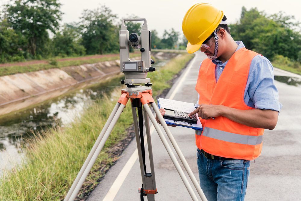Man Wearing A Yellow Hard Hat Is Looking At A Clipboard — Surveyor In Canowindra, NSW