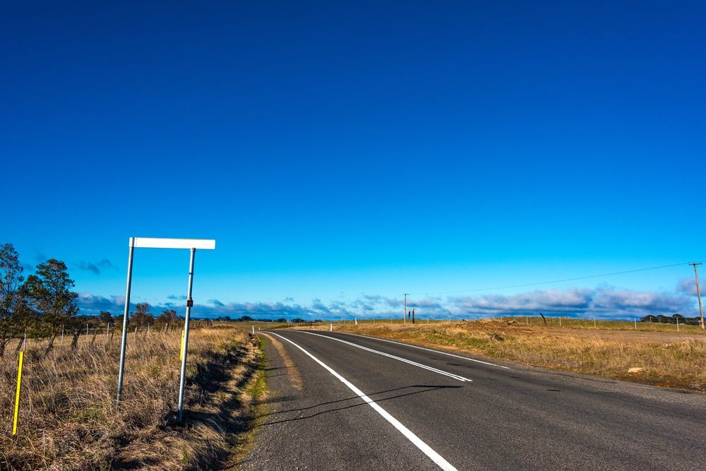 Road With A White Sign On The Side Of It and Blue Clear Sky in Background — Surveyor In Young, NSW
