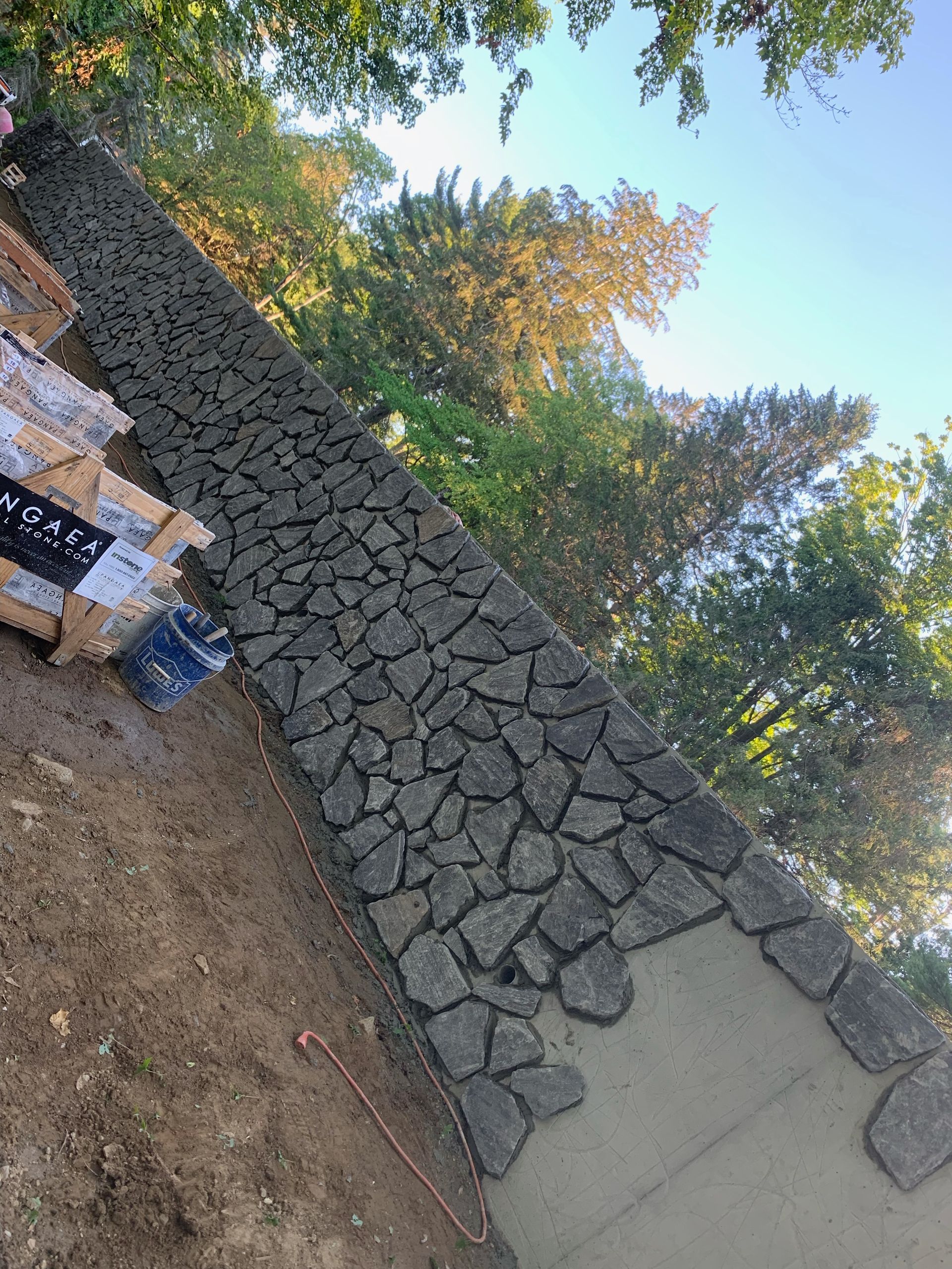 A stone wall is being built in a yard with trees in the background.