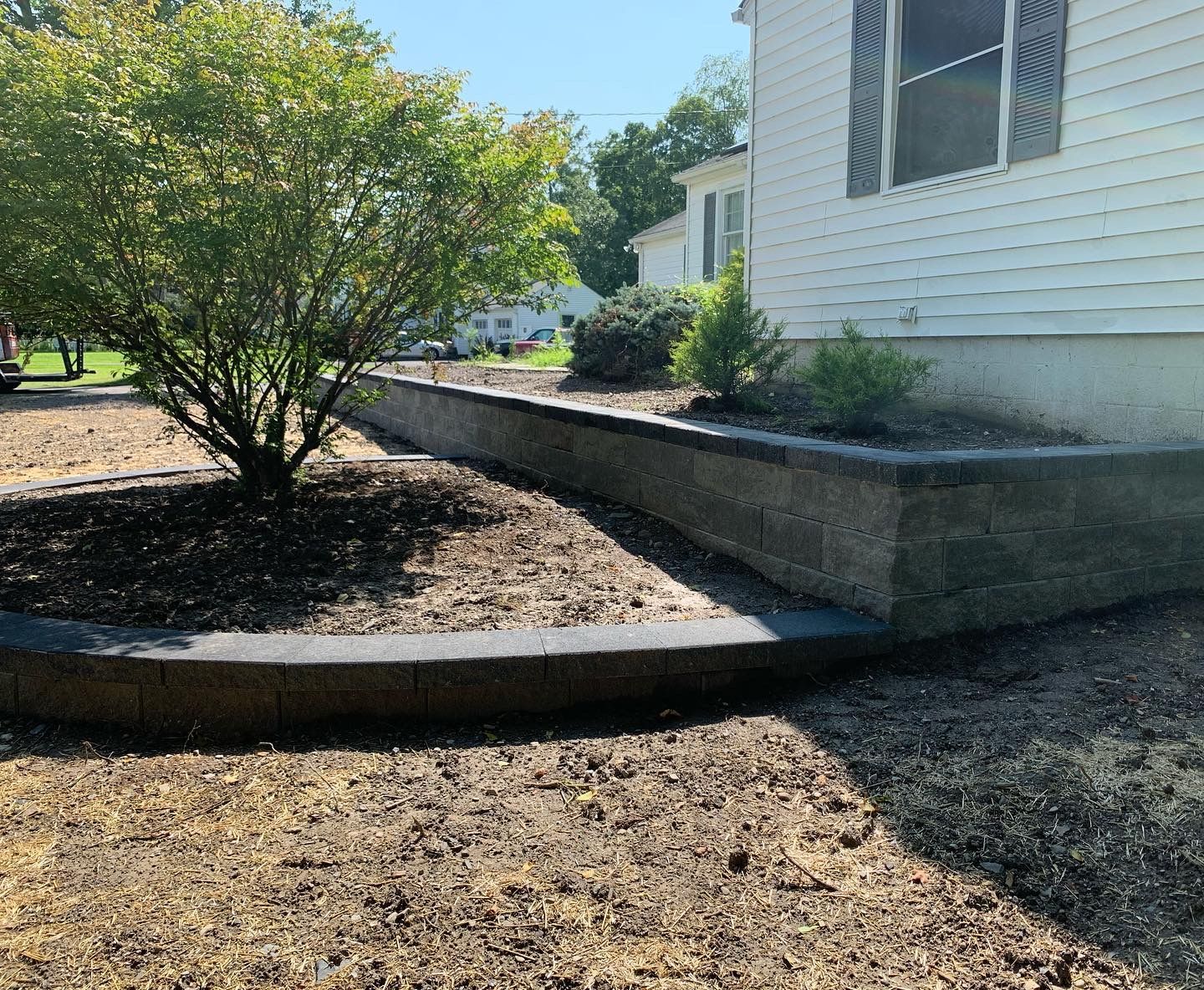 A house with a brick wall and a bush in front of it.
