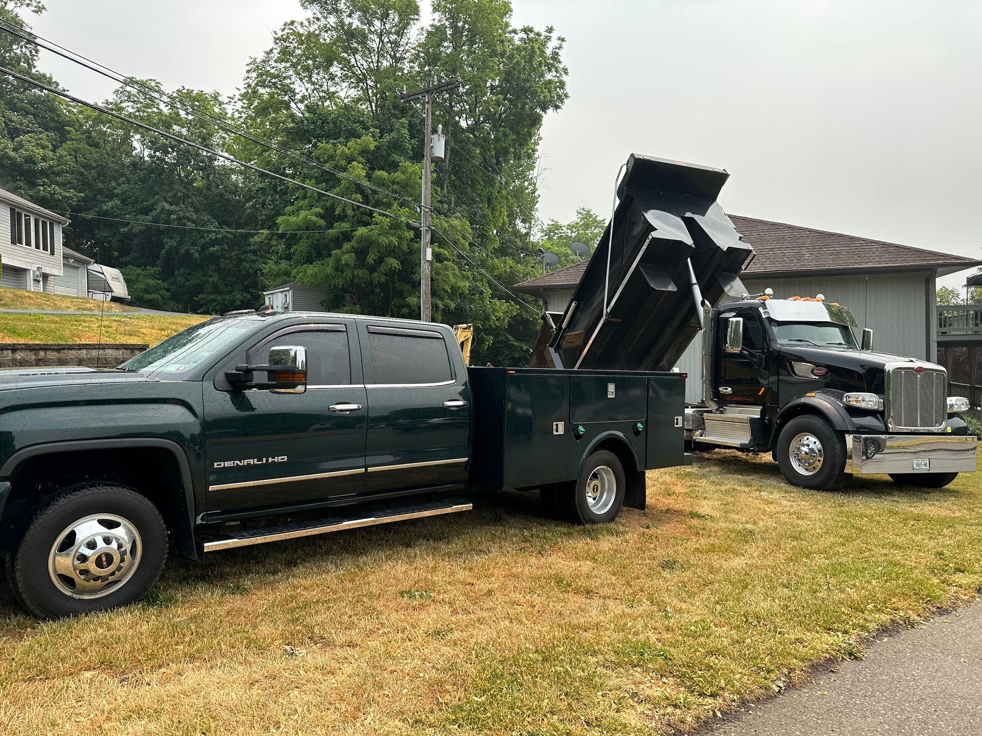 Two dump trucks are parked next to each other in a grassy field.