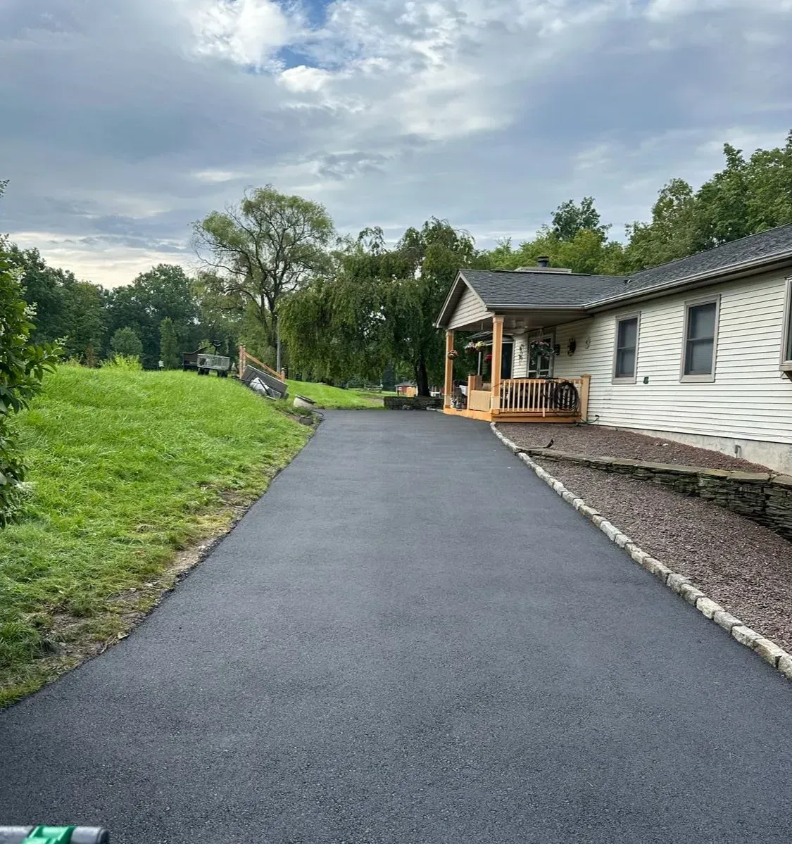 A driveway leading to a house with a porch surrounded by trees.