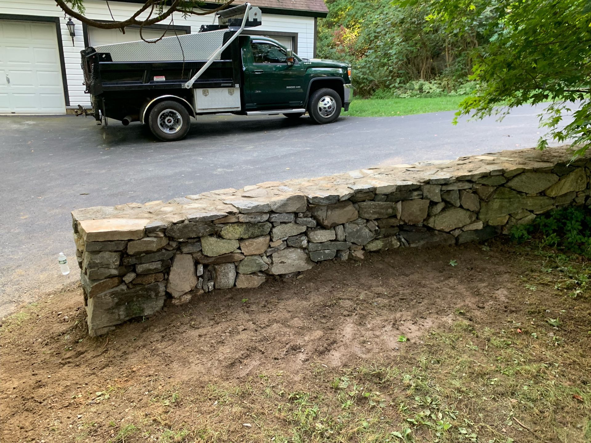A dump truck is parked in a driveway next to a stone wall.