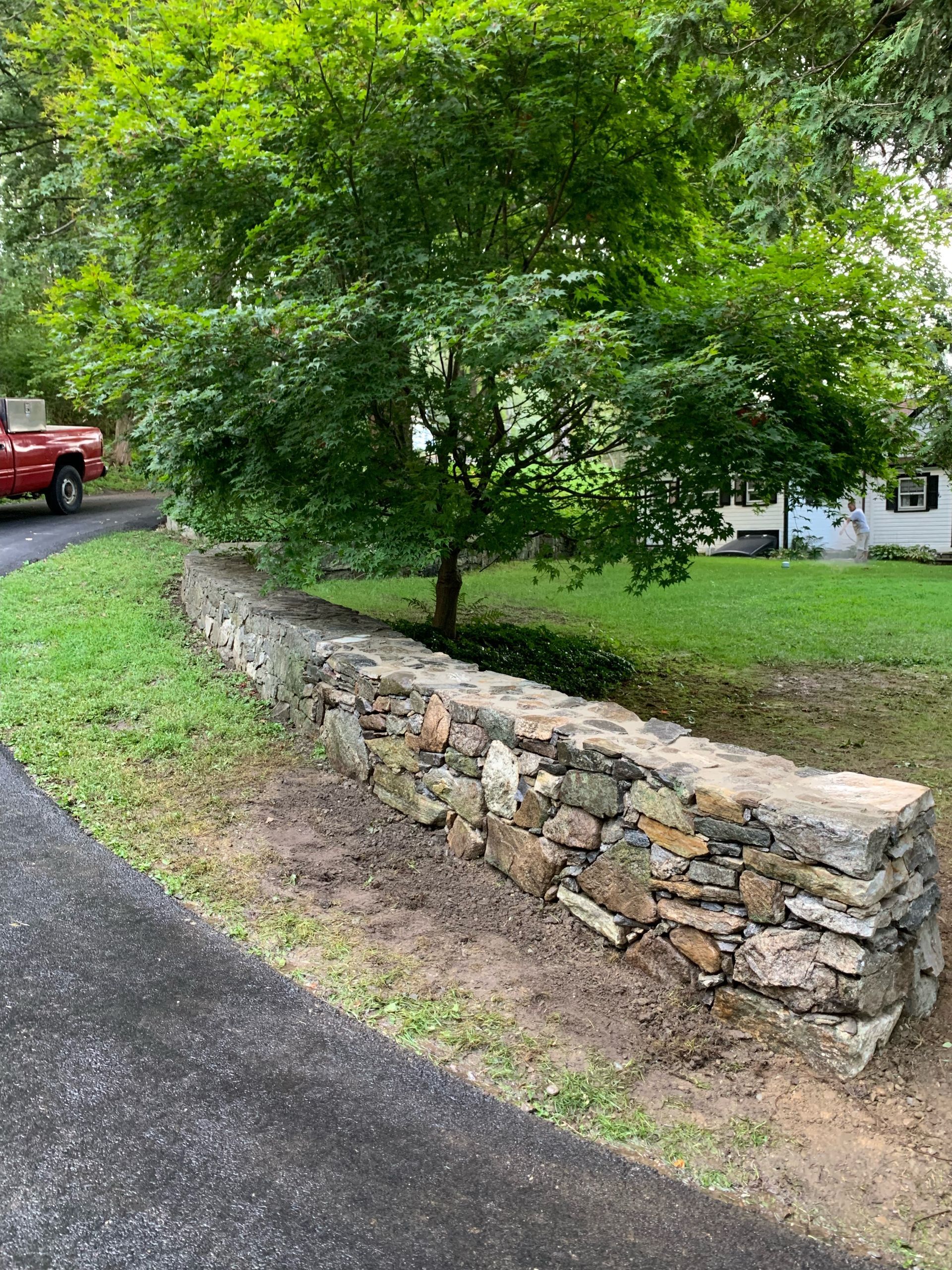 A red truck is parked next to a stone wall.