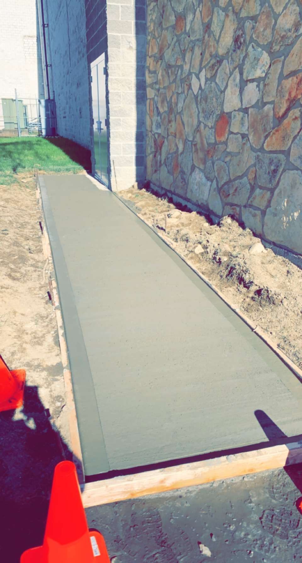 A concrete walkway is being built in front of a stone wall.