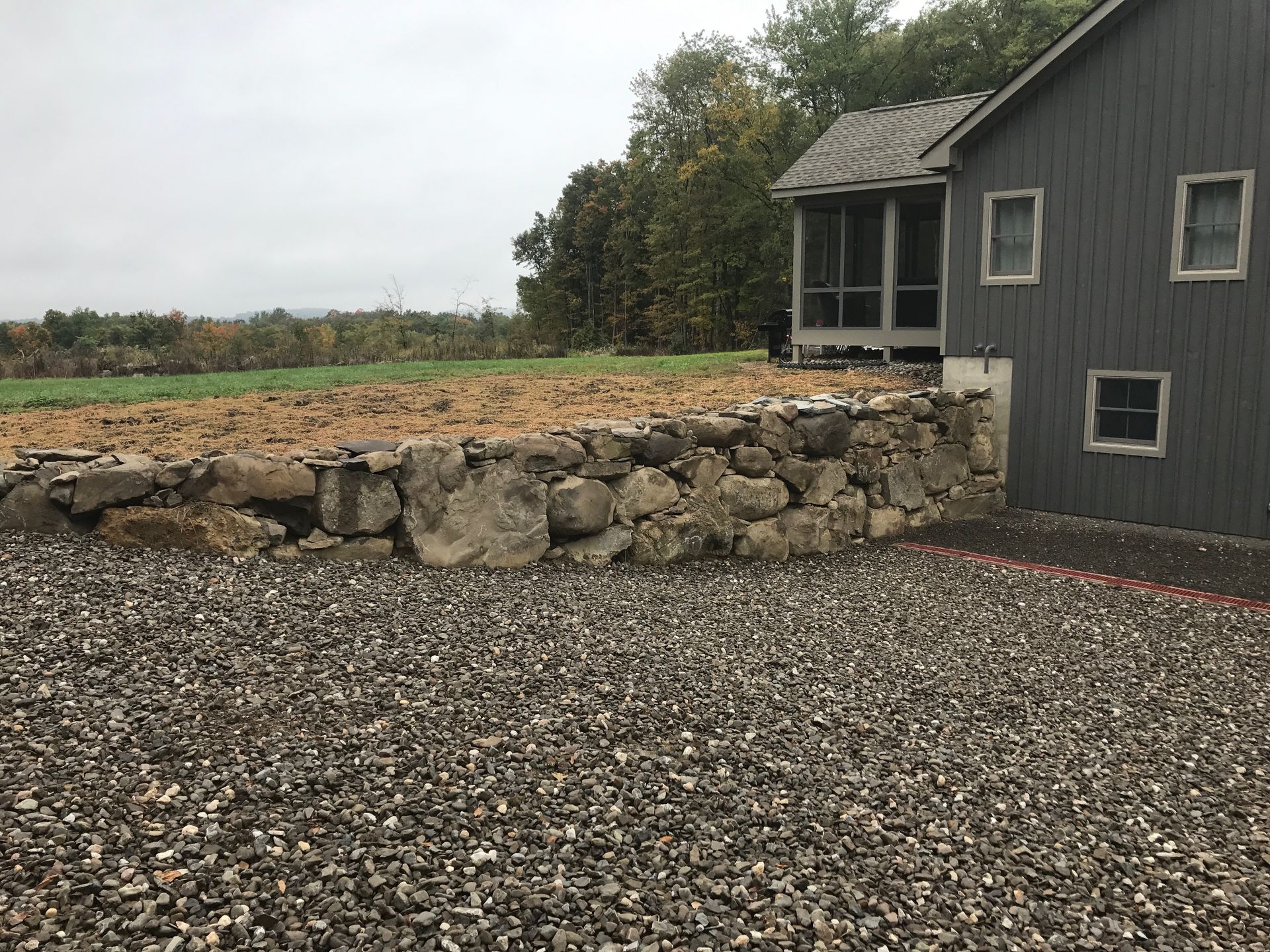 A house with a screened in porch and a stone wall in front of it.