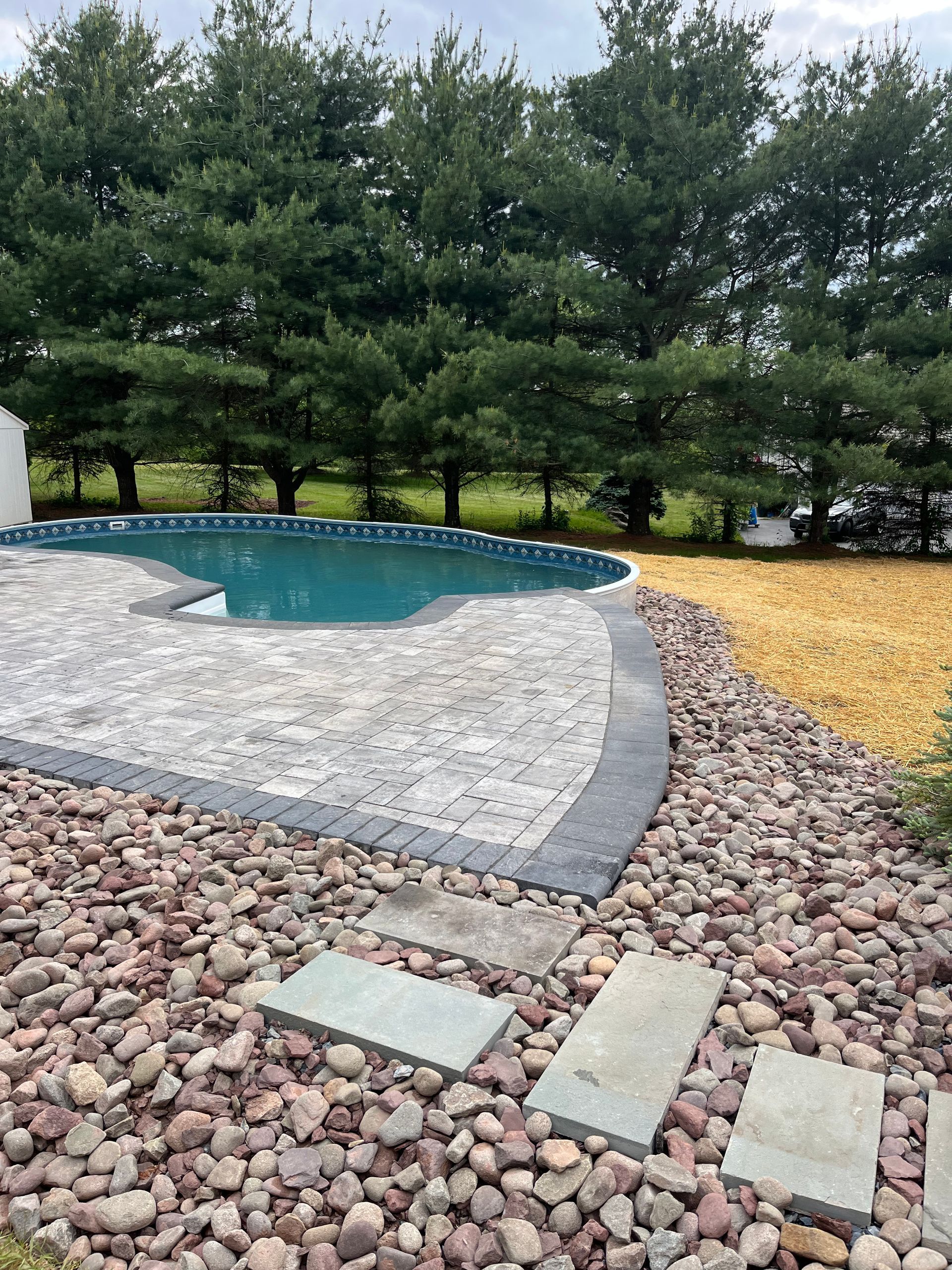 A swimming pool surrounded by rocks and trees in a backyard.