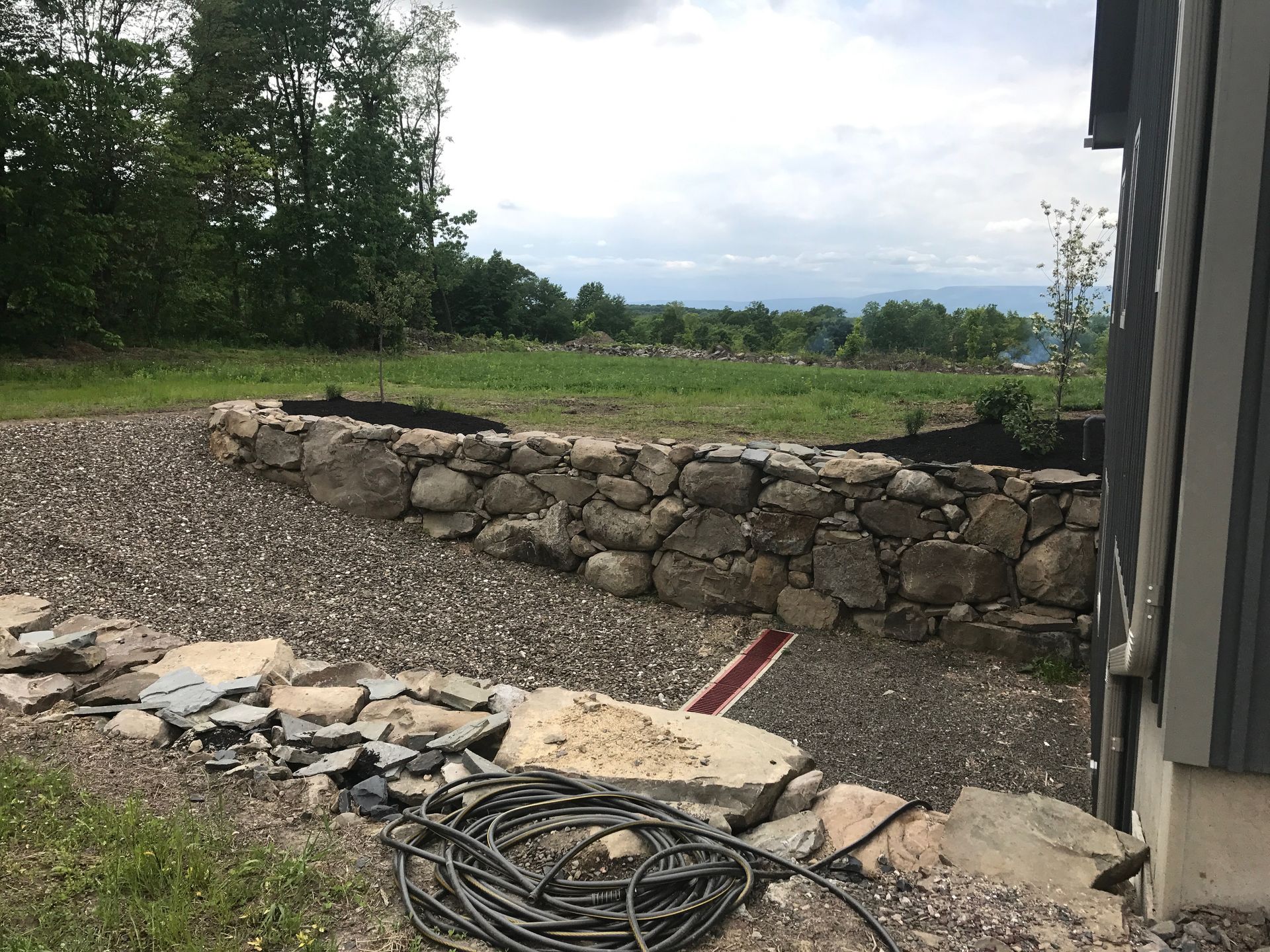 A hose is sitting on the ground next to a stone wall.