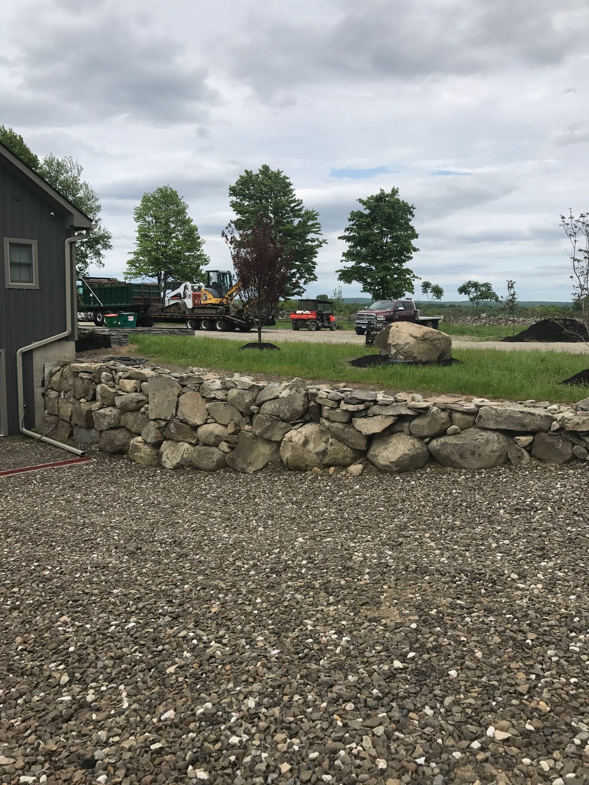 A gravel driveway with a stone wall and a house in the background