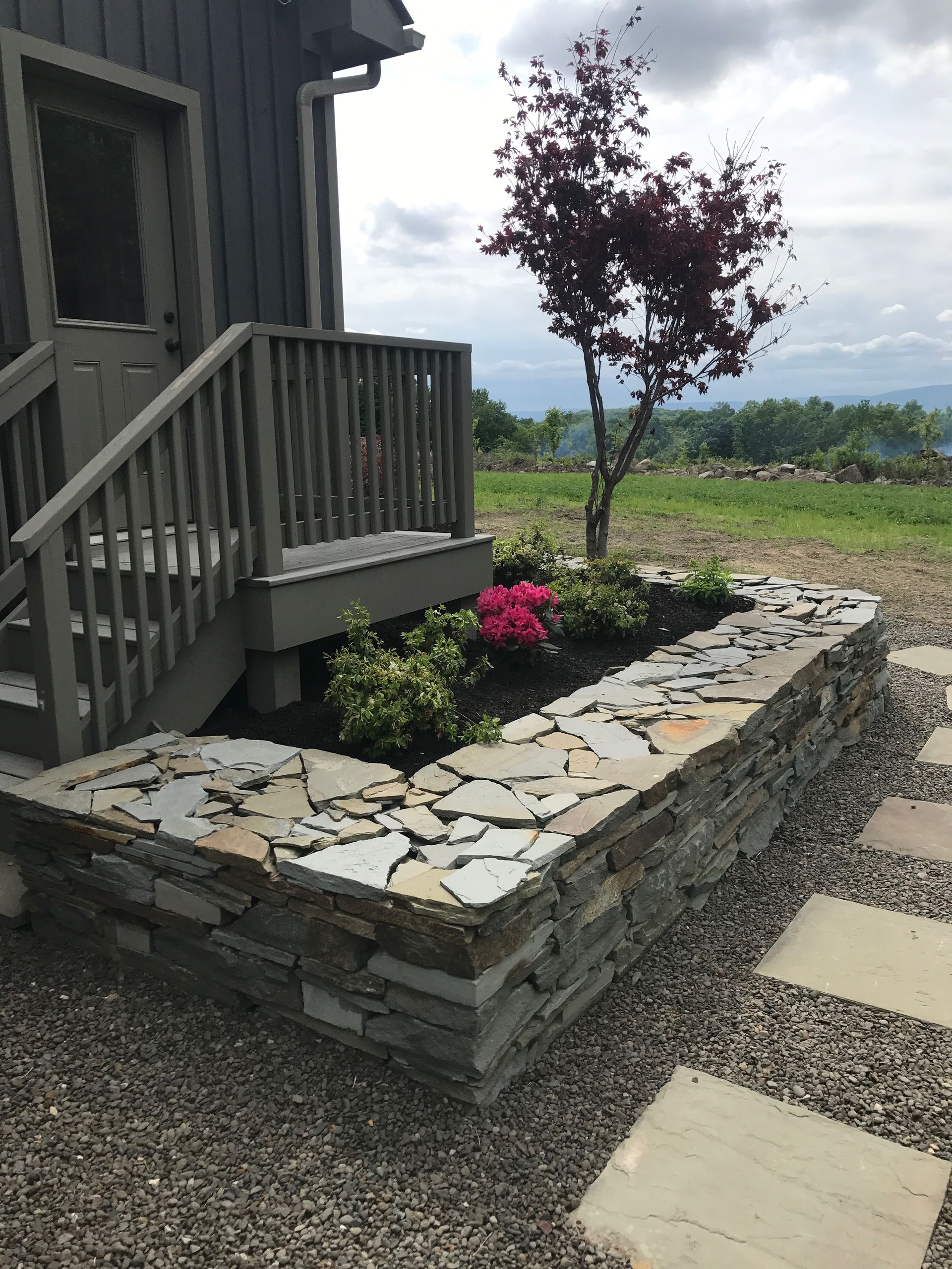 A stone wall with flowers and a tree in front of a house