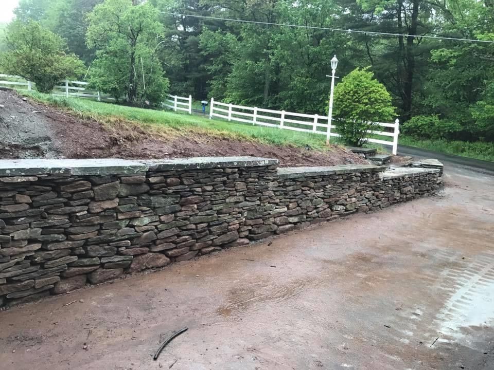 A stone wall is being built next to a dirt road.