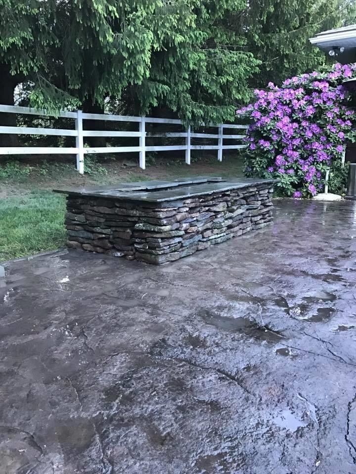 A stone wall is sitting on top of a concrete patio next to a white fence.