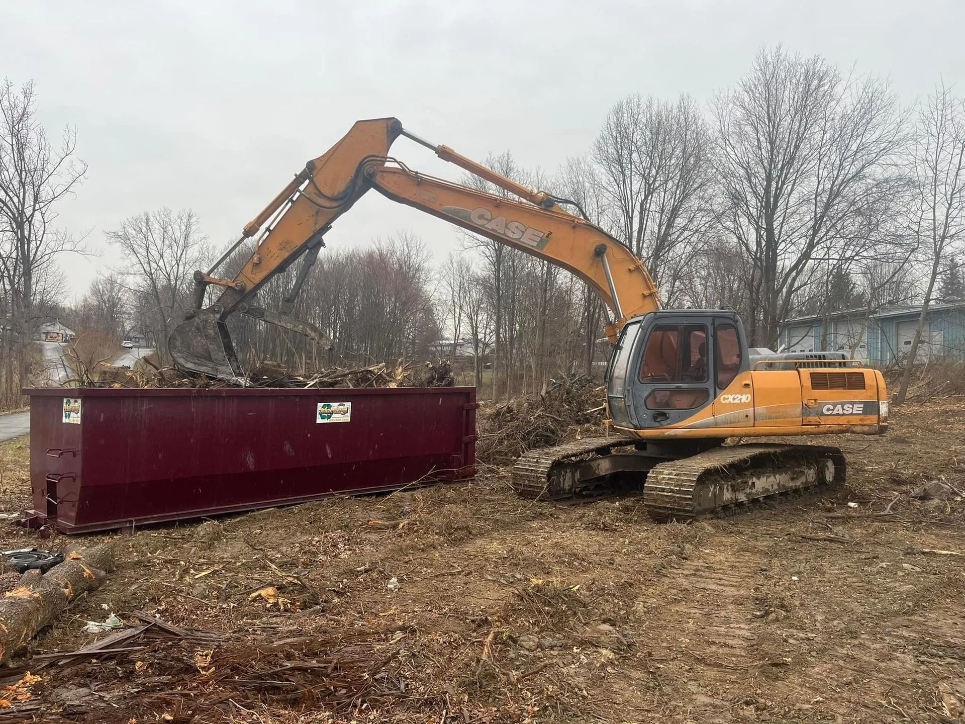 A large excavator is loading a dumpster in a field.