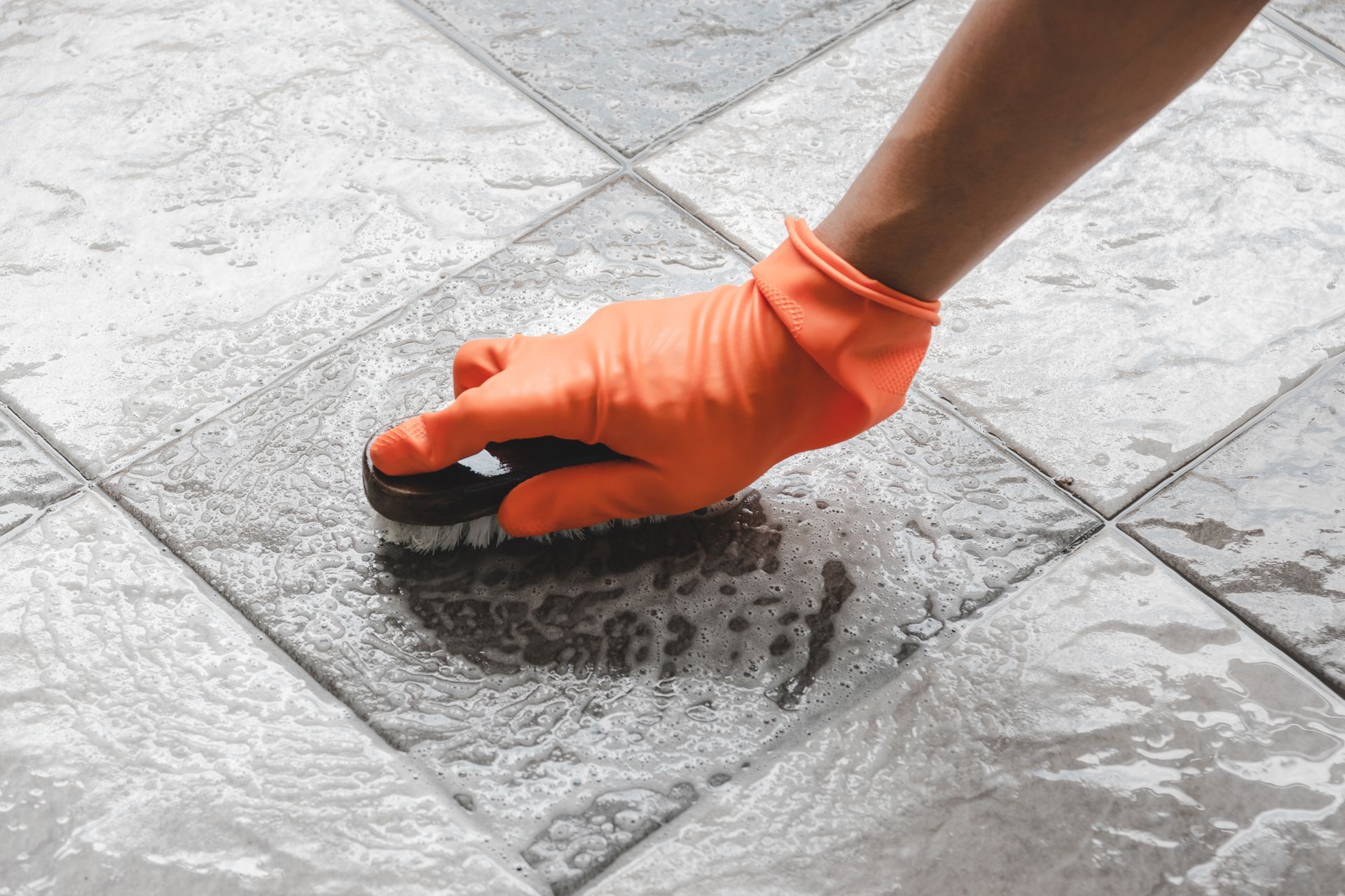 a person wearing orange gloves is cleaning a tile floor with a sponge