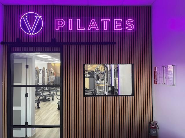 V pilates studio with a neon sign on the wall.