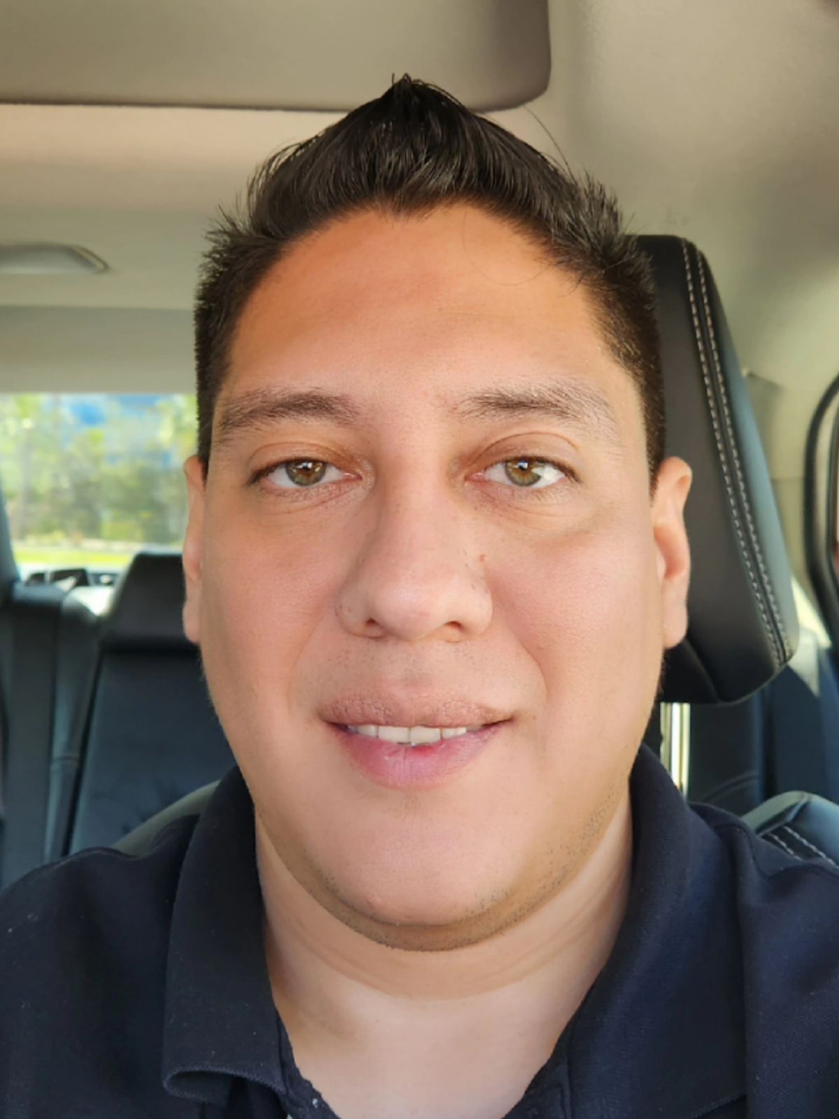 Man with short dark hair smiles, in a car.