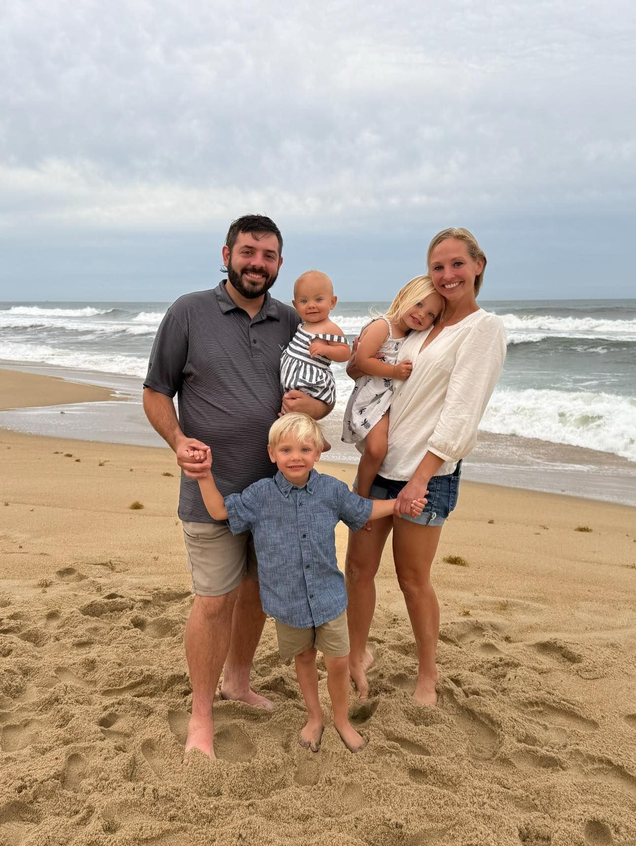 Family of four standing barefoot on a beach with waves in the background, smiling at the camera | Medina’s Ace Auto