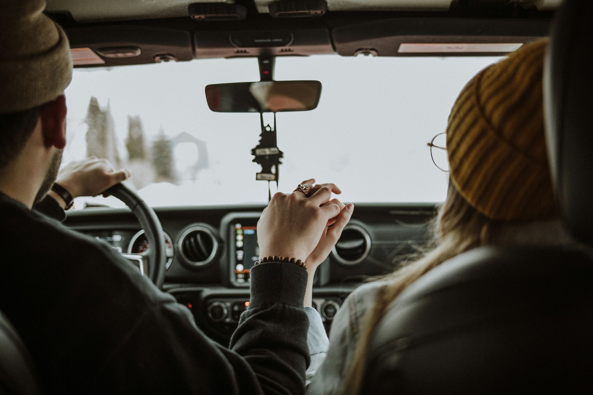 A man and a woman are holding hands while driving a car.