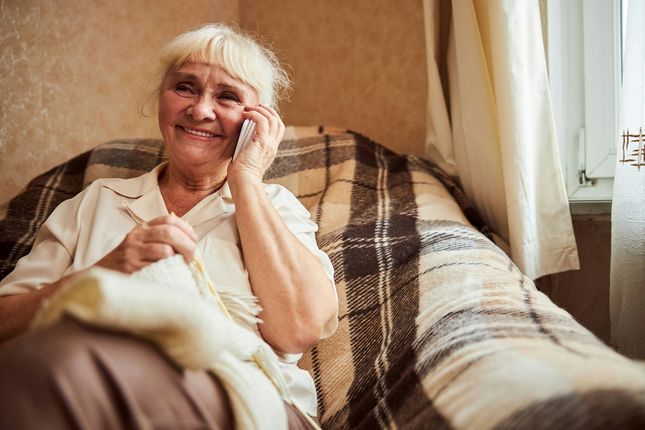 An elderly woman is sitting on a couch talking on a cell phone.