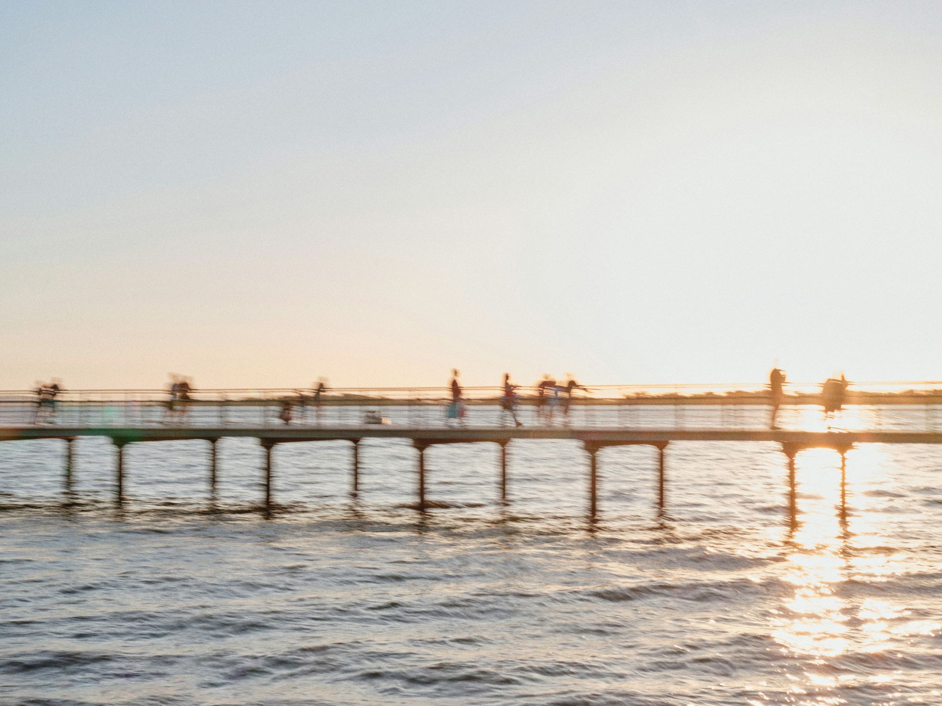 A group of people are standing on a pier overlooking a body of water at sunset.