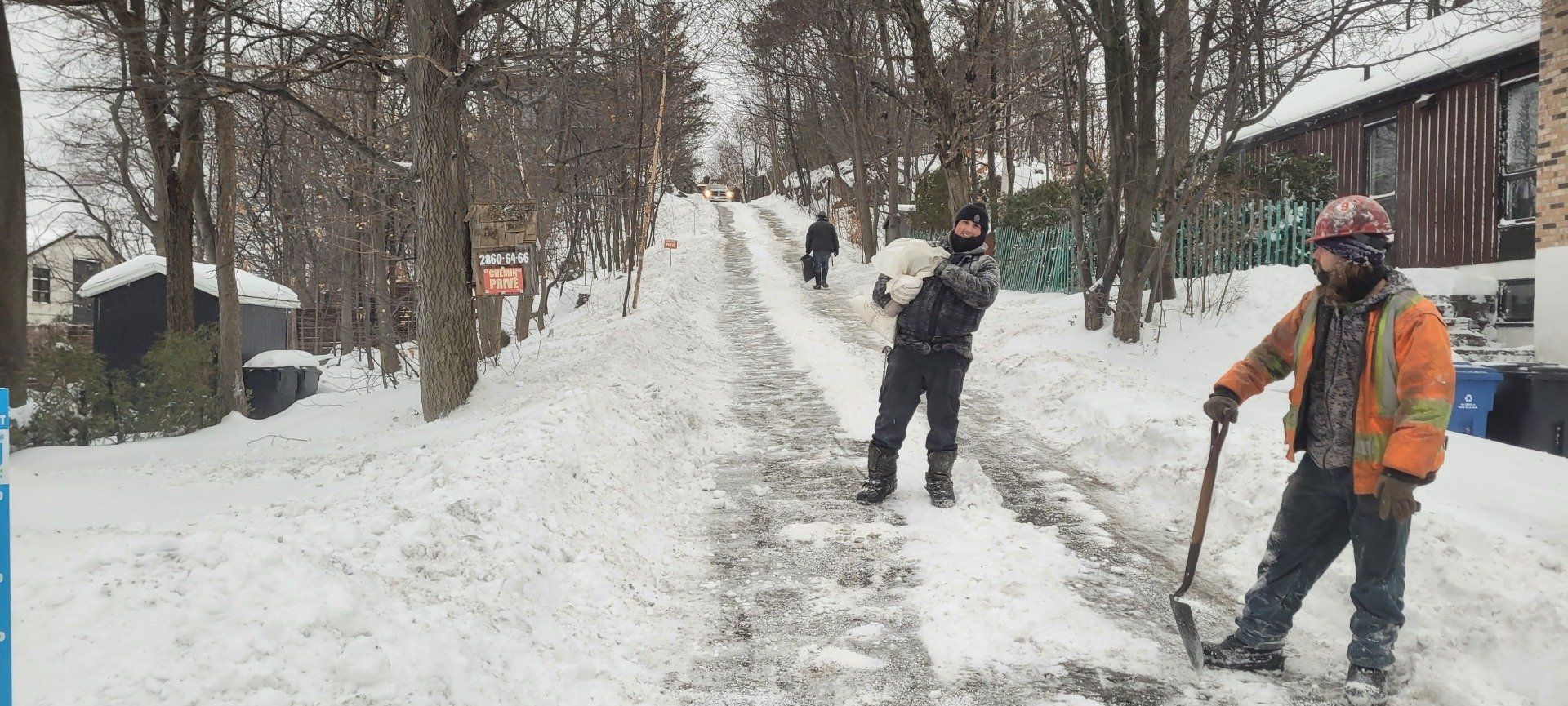 Deux hommes pelletent de la neige sur une route enneigée.