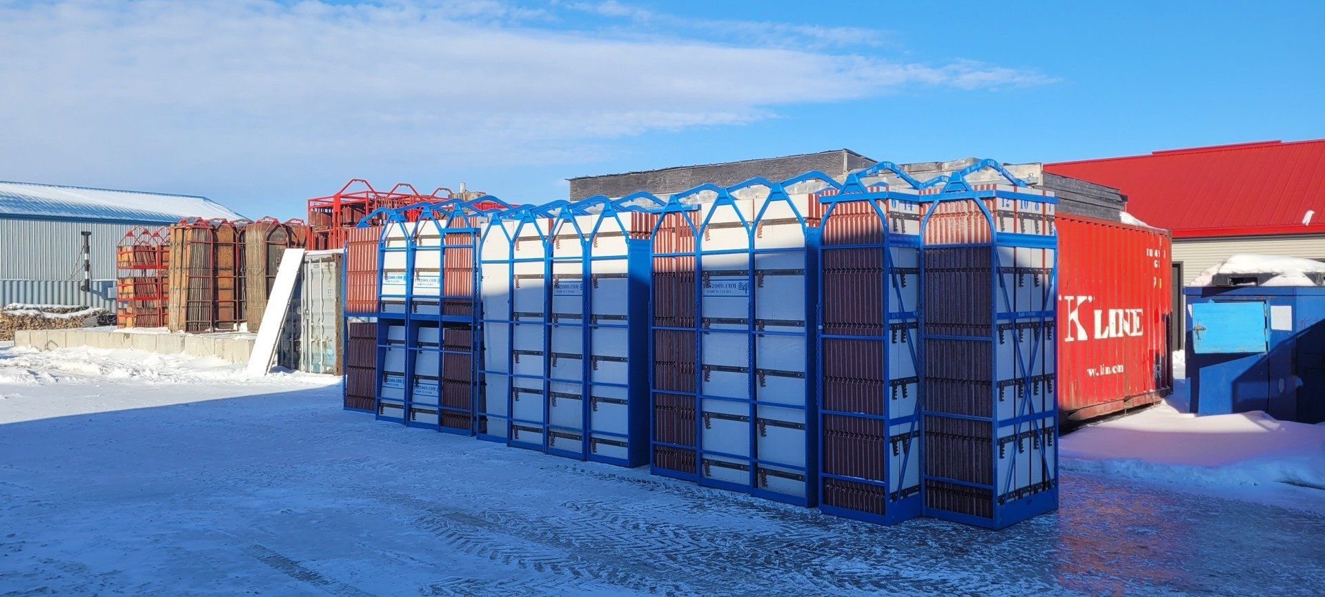 Une rangée de conteneurs maritimes repose dans la neige devant un bâtiment.