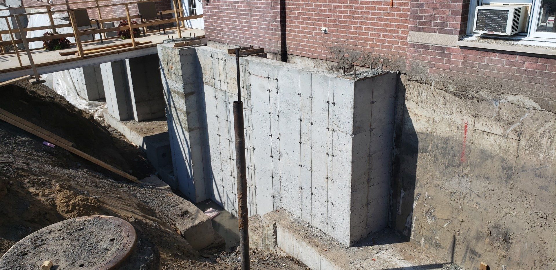 Murs de fondation en béton en construction à côté d'un bâtiment en briques. Le sol a été excavé autour des murs.
